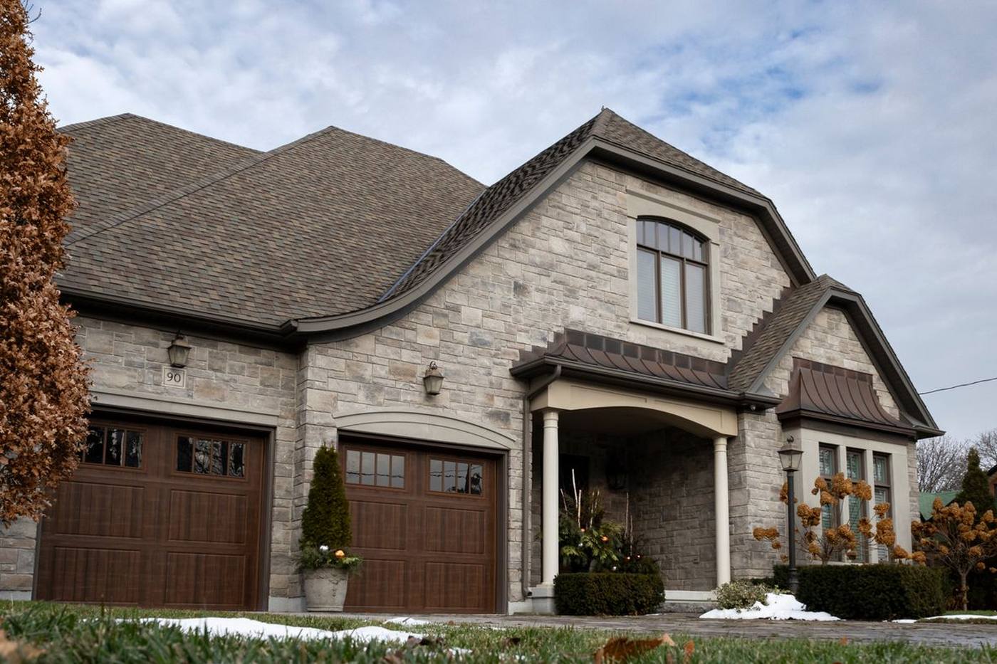 Stone-fronted home with two brown carriage-house garage doors replacing a dated single door