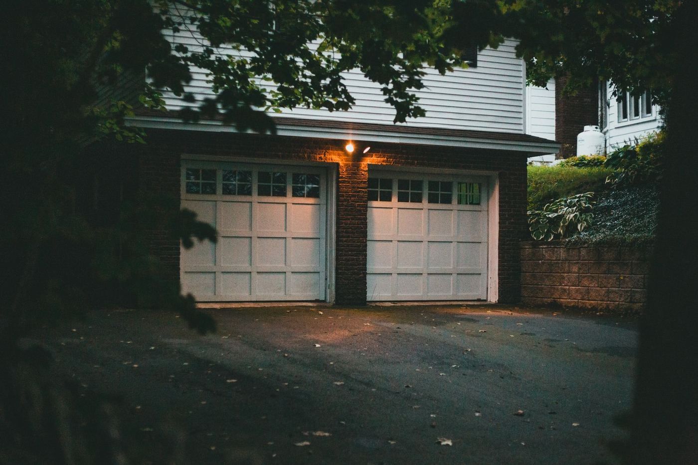 Residential garage doors lit from inside at dusk with the driveway in shadow