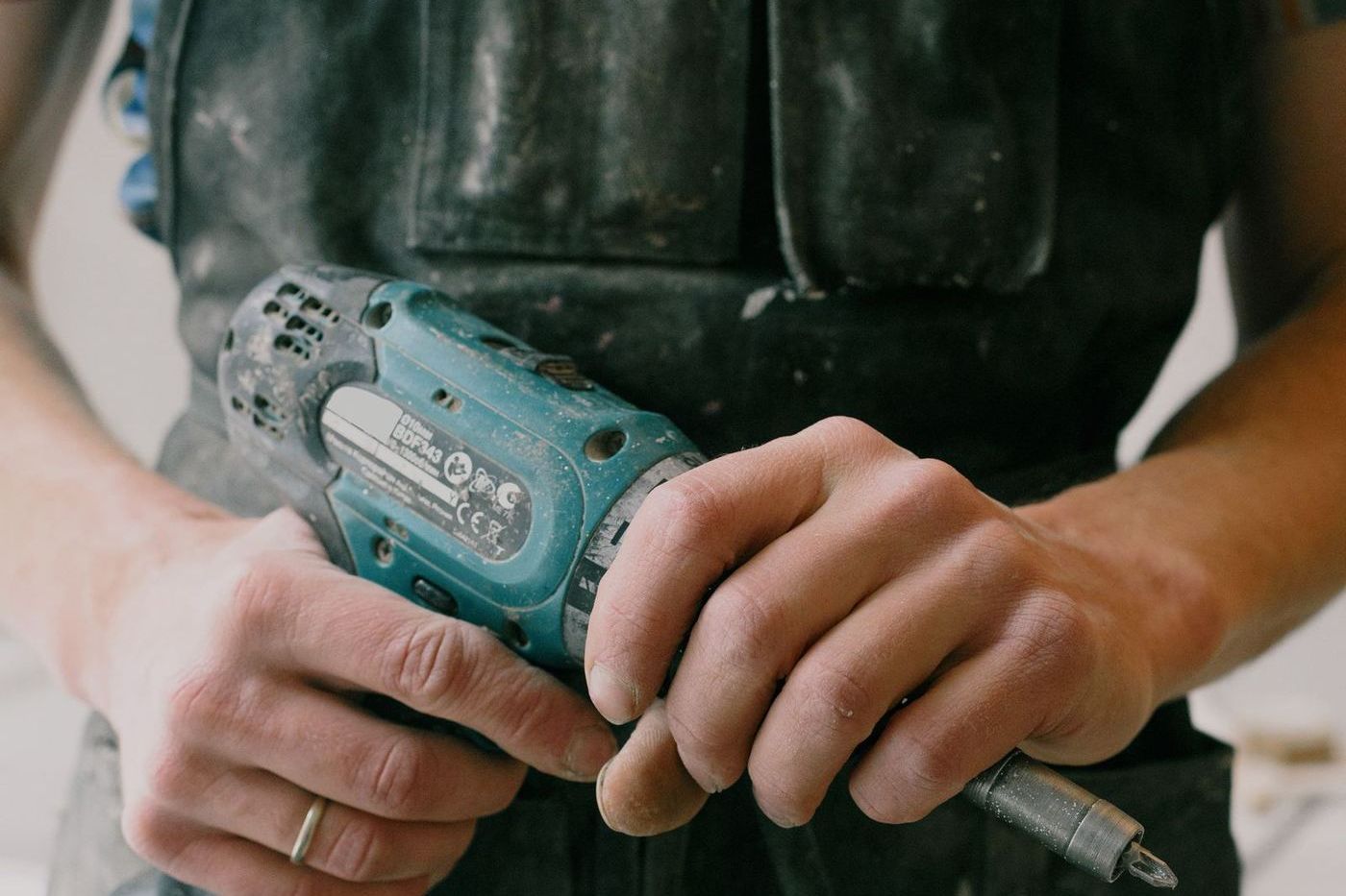 Tradesperson in work overalls holding a cordless drill ready to service door hardware